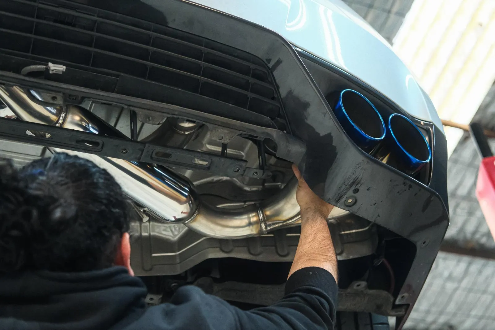 Rear bumper removed during HKS Legamax Premium install on R35 GT-R showing stainless piping and blue burnt tips