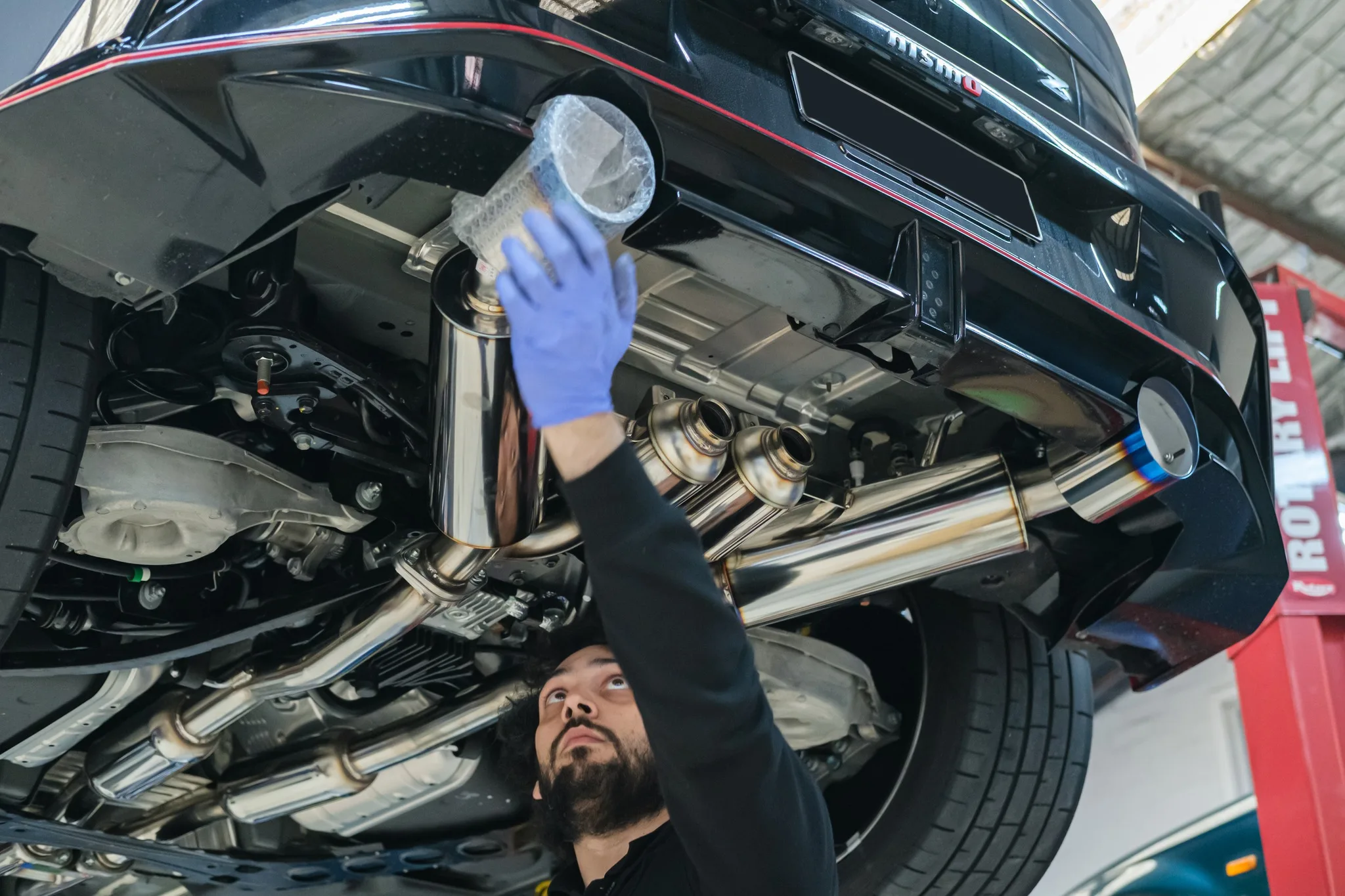 Revzone technician fitting HKS Full Dual Muffler exhaust to Nissan Z NISMO on the hoist